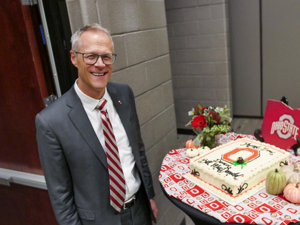 Dean and director William MacDonald stands next to a cake celebrating his 20 years of service. 