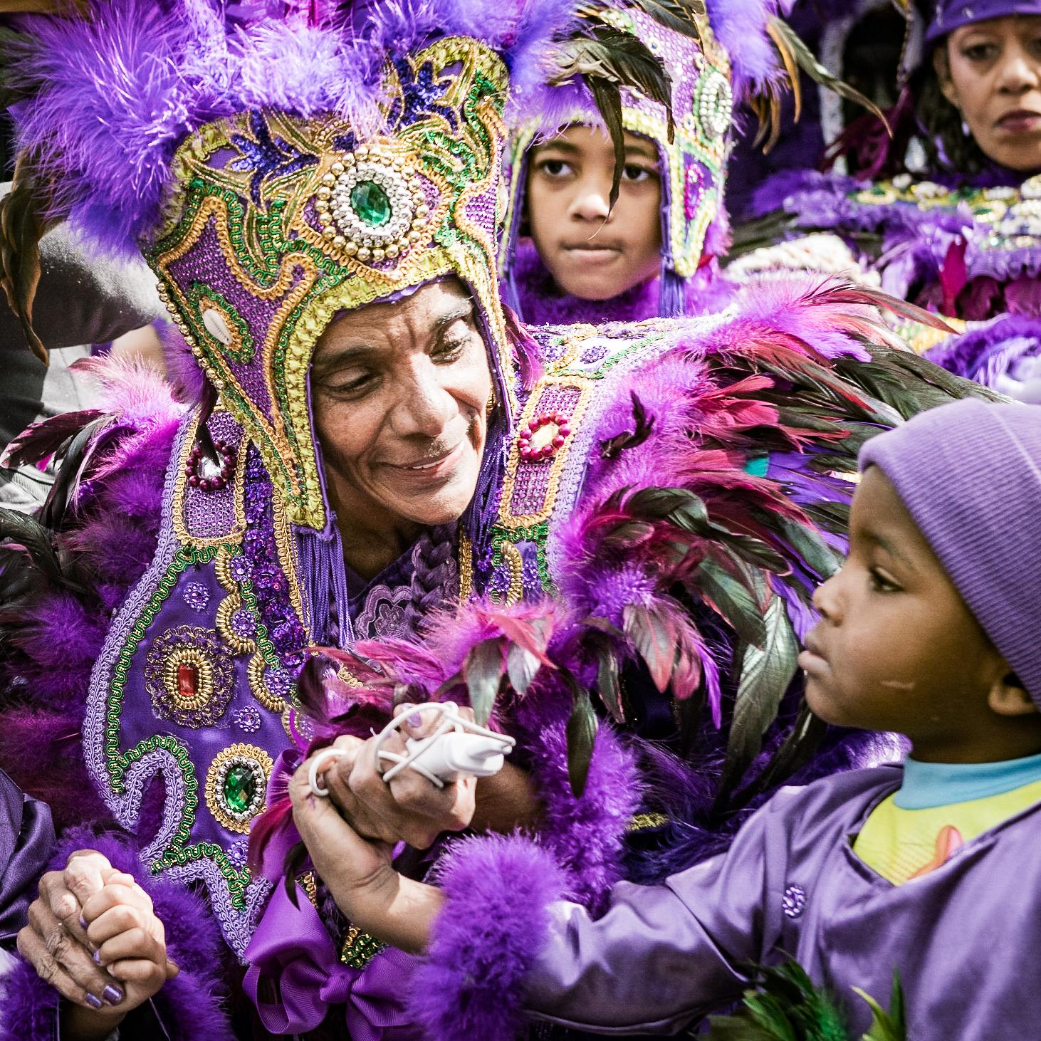 A person dressed in a beaded and feathered costume surrounded by children in similar costume.