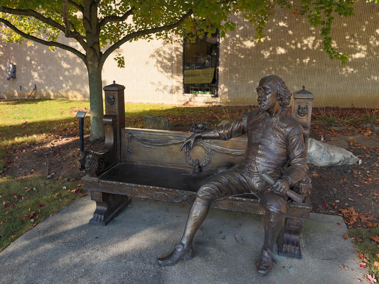 A bronze statue of William Shakespeare seated on a bench.