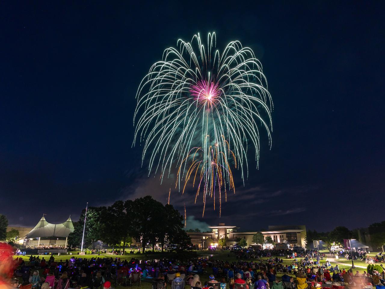 A firework fills the night sky over the Warner Center as onlookers fill the campus grounds