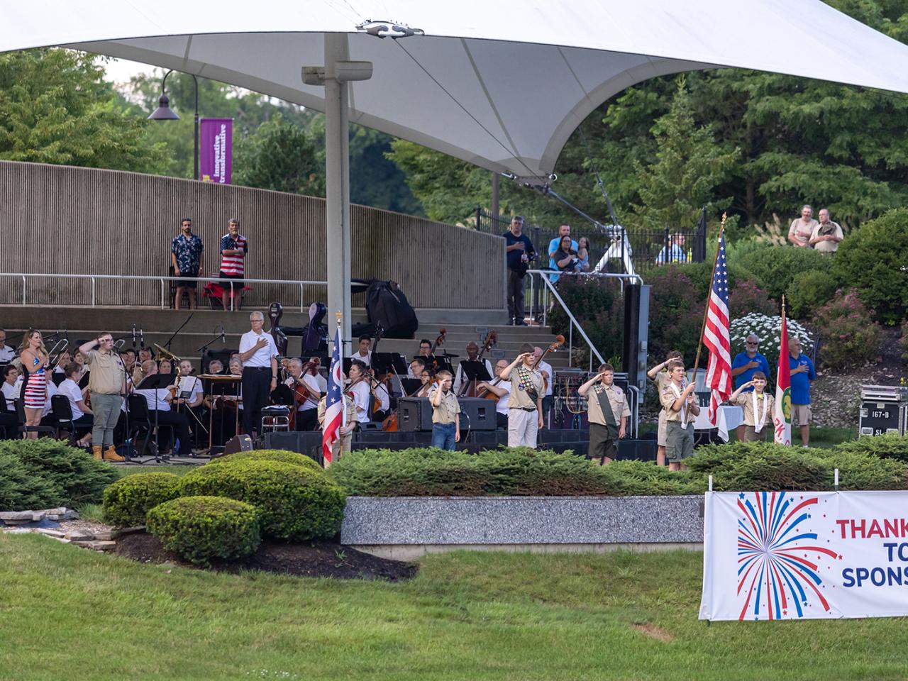 A boy scout holds the American flag while the rest of the troop salutes from the amphitheater.