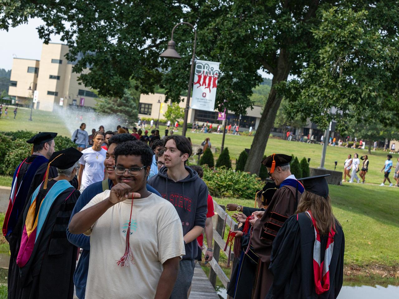 A student holds up the tassel he received after participating in the bridge walk while students are lined up behind him.