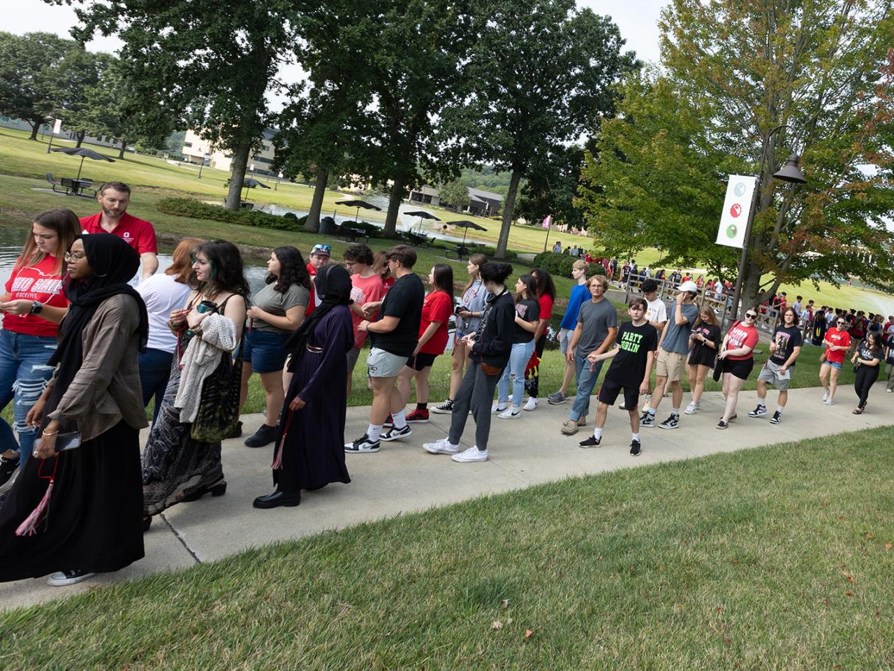A crowd of students walk on the sidewalk on campus. 