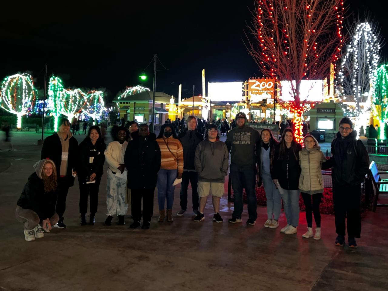 Students stand in front of trees lit for Christmas at the Columbus Zoo and Aquarium.