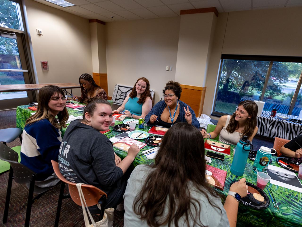 Students sit around a table with painting a canvas of Brutus Buckeye.