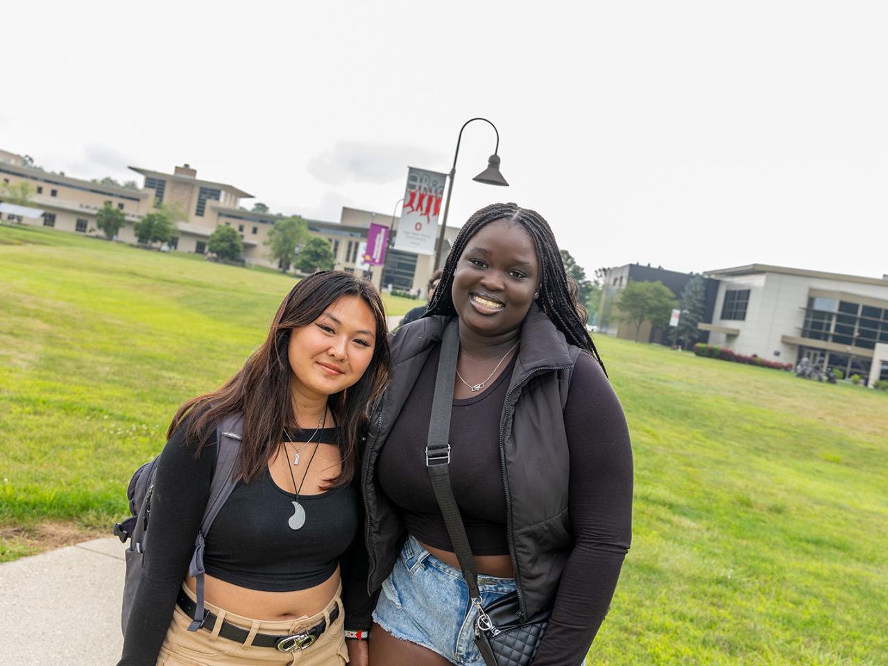 Two students stop to smile and pose for a photo on the campus lawn. 
