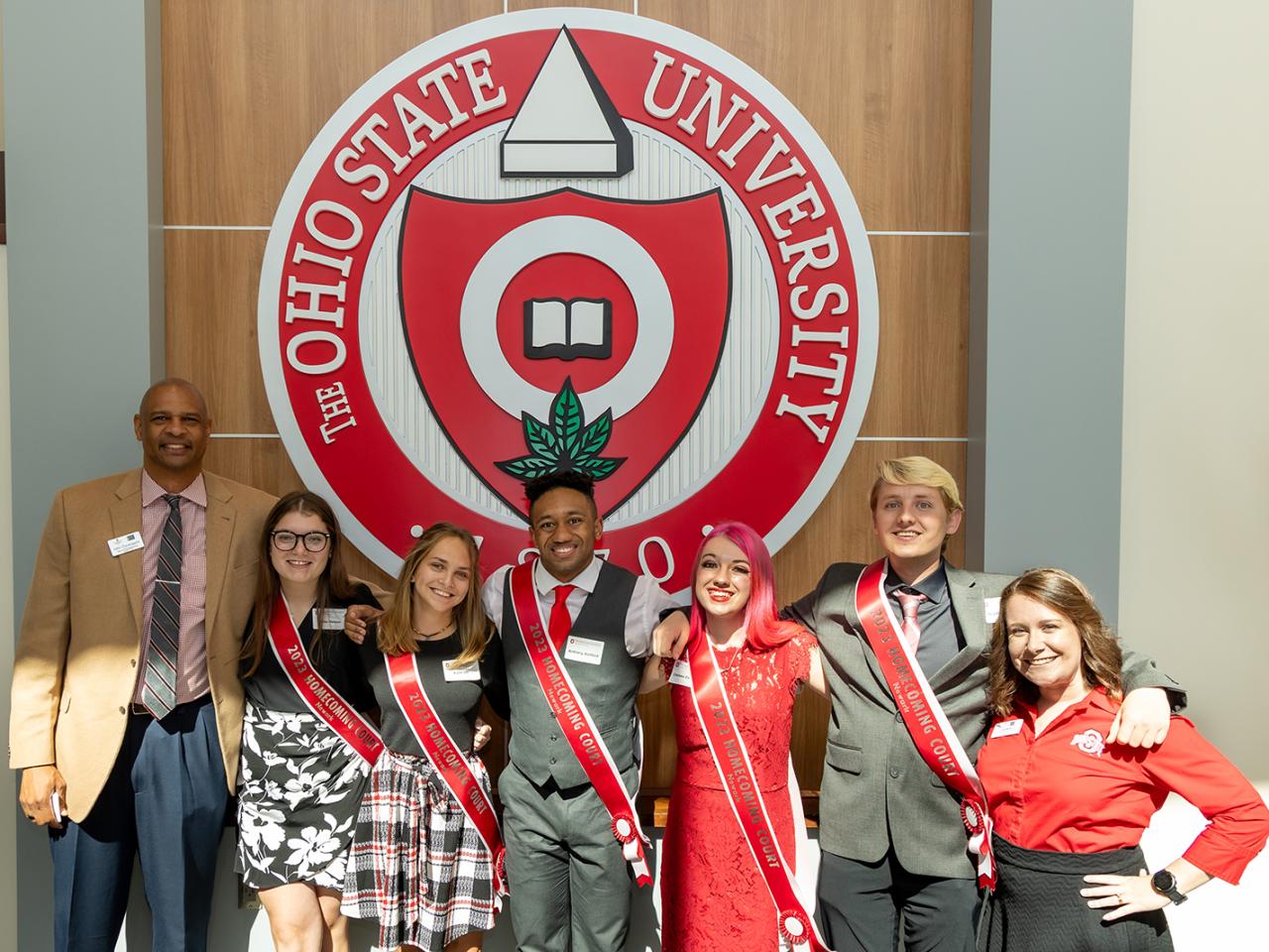 The Homecoming Court members and Office of Student Life staff members stand under the university seal in the Longaberger Alumni House.