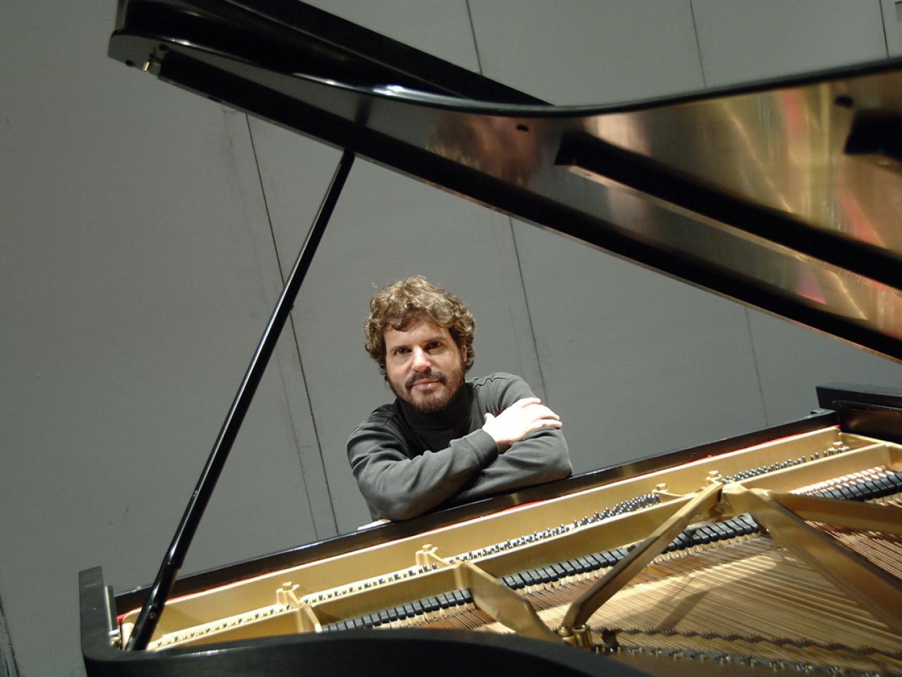 Steven Glaser sits behind a piano with his arms crossed, resting on top.