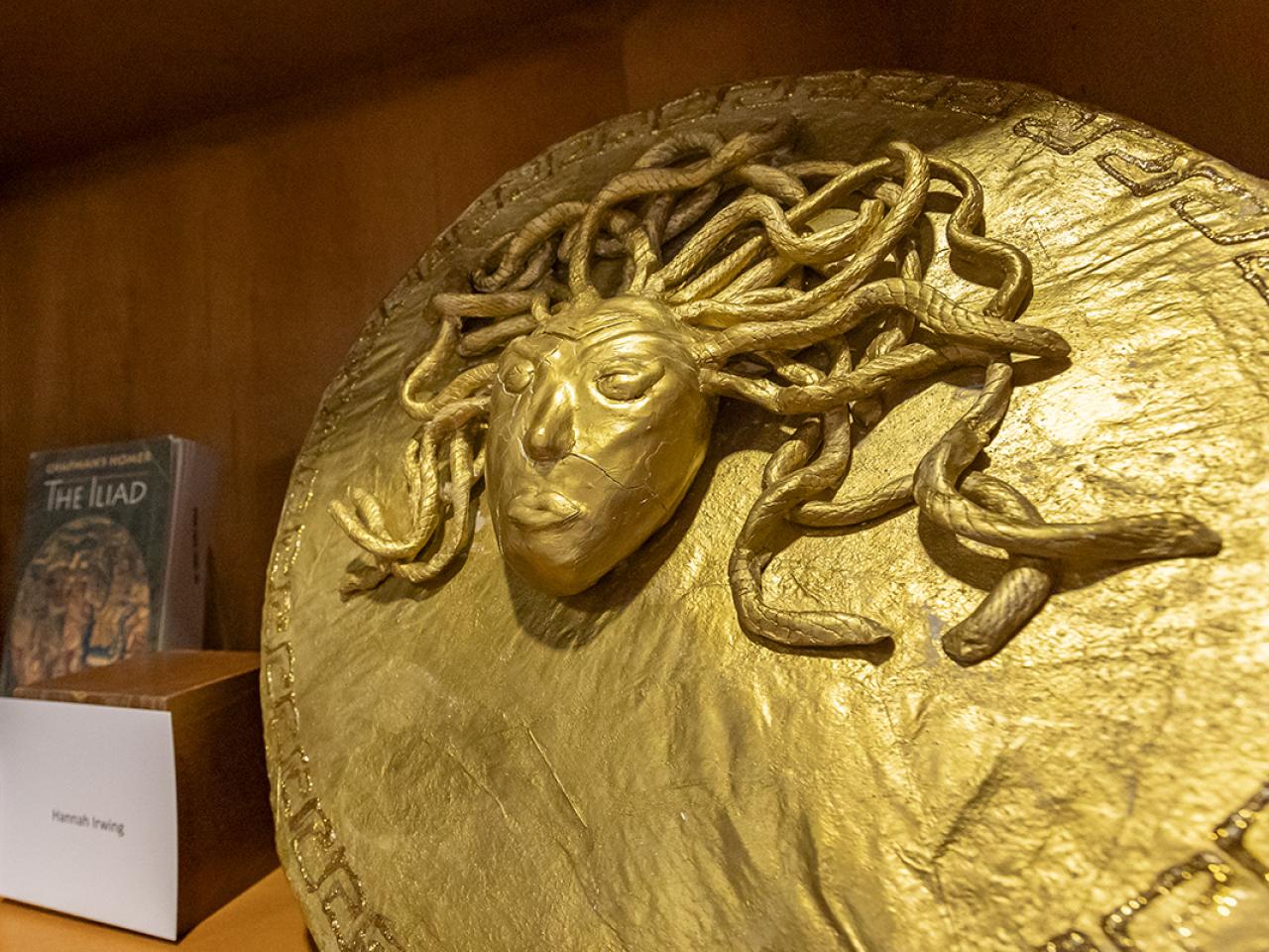 A shield with the head of Medusa covered in gold created by a student. 