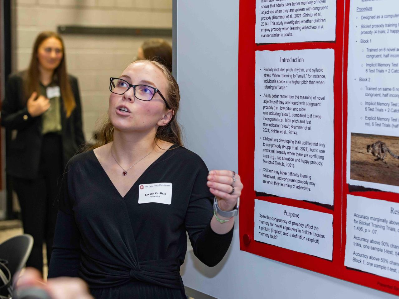 A student stands next to her poster presentation talking to a spectator. 