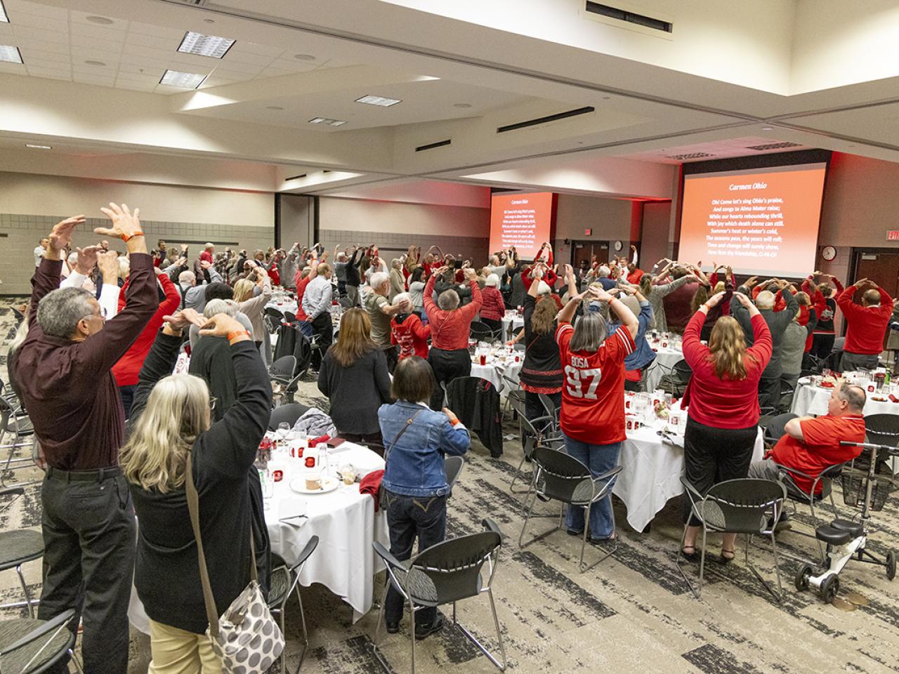 Attendees raise their arms above their heads in an O formation.