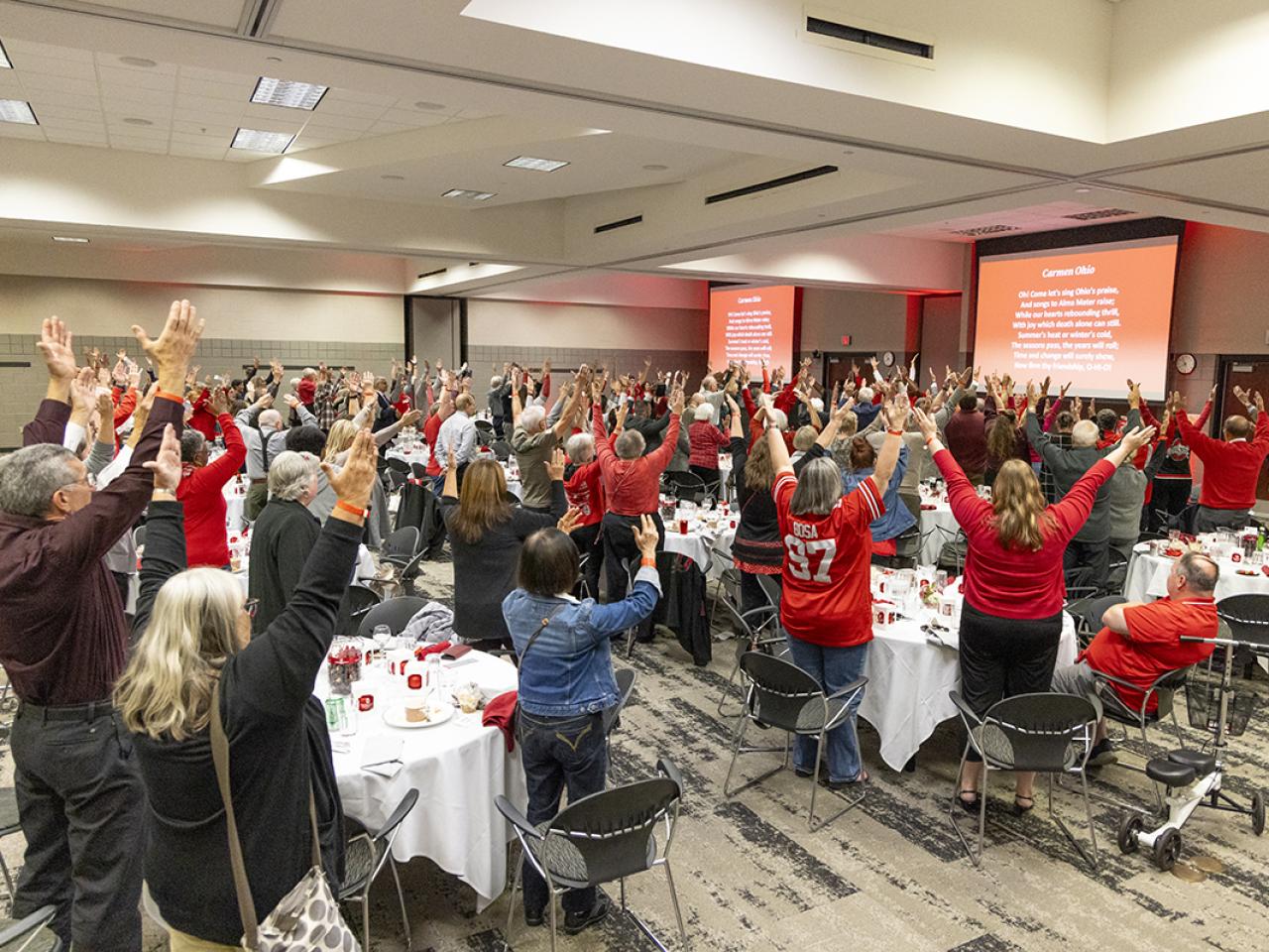 Attendees raise their arms above their heads in an H formation.
