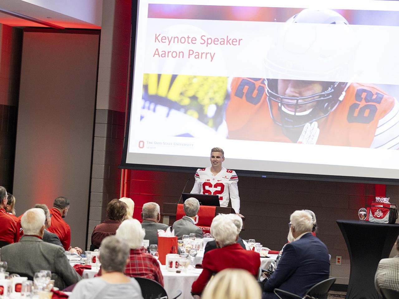 Former Ohio State football player and keynote speaker Aaron Parry stands at a podium addressing the audience at the Alumni Homecoming celebration.