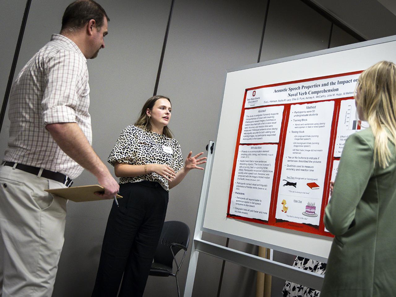 A student stands next to her poster presentation talking to a spectator. 