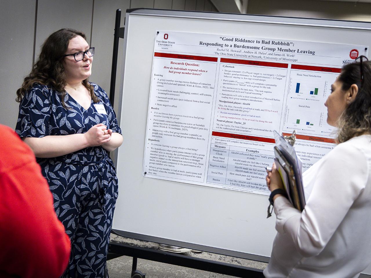 A student stands in front of her research poster presenting to a couple onlookers.