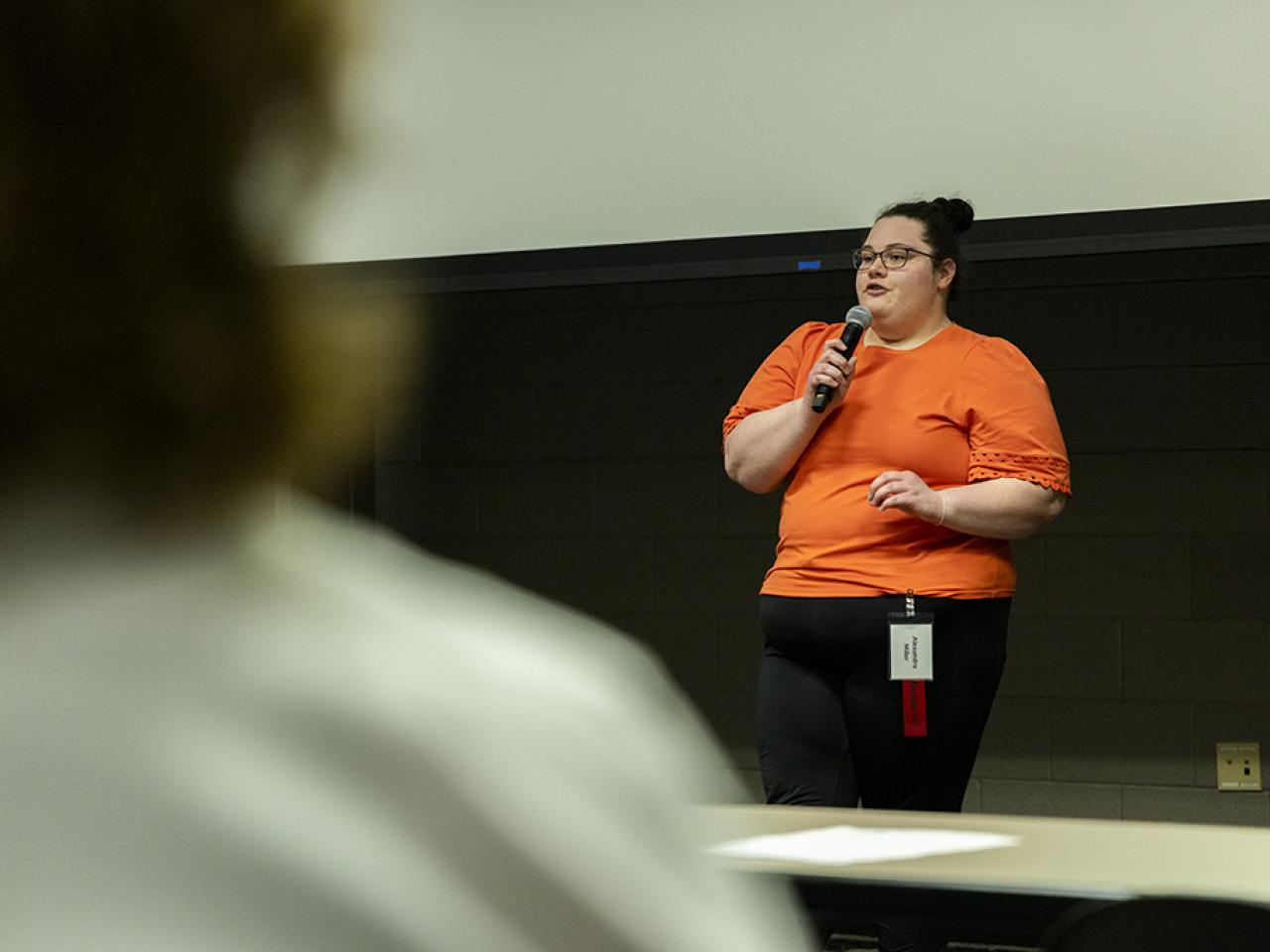 Alexandra Miller speaks into a microphone as she gives an oral presentation to an audience at the Student Research and Creative Inquiry forum.