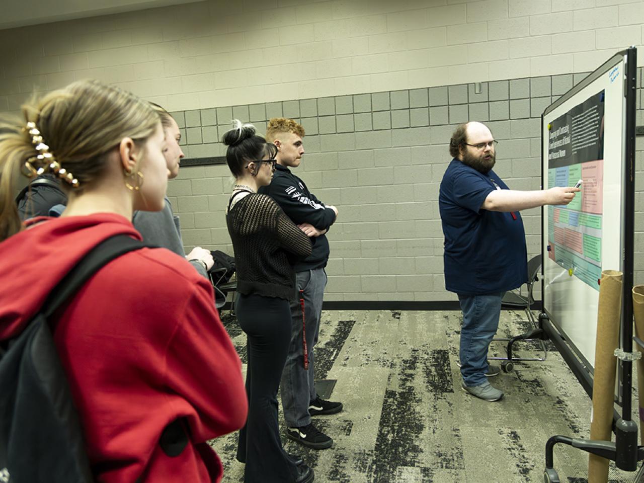Andrew Hinton points to his poster as students watch his presentation during the Student Research and Creative Inquiry Forum.