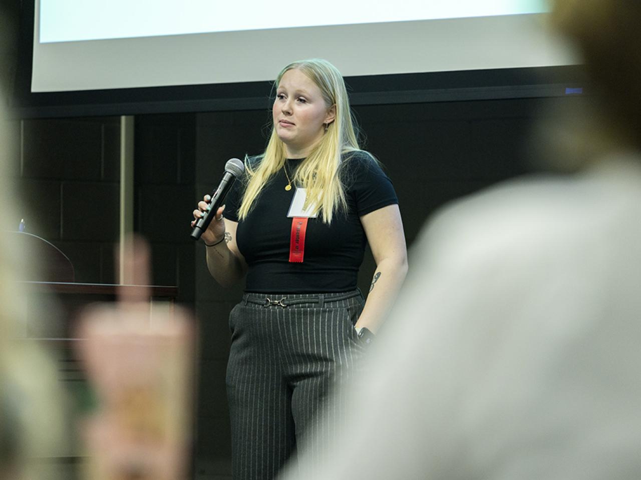 Anna Mays holds a microphone looking into an audience as she gives an oral presentation during the Student Research and Creative Inquiry Forum.