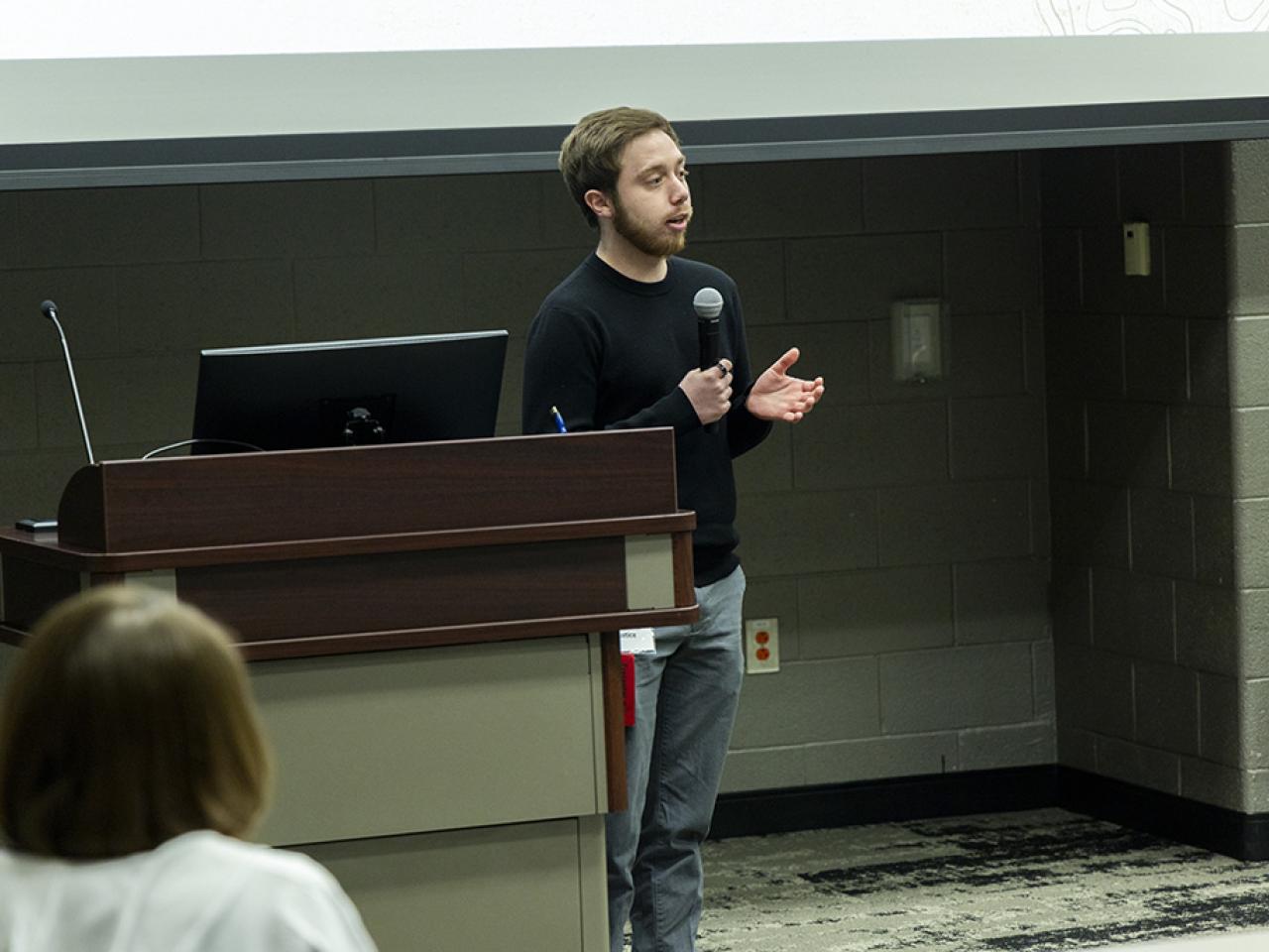 Brenden Justice stands at a podium speaking into a microphone during his oral presentation at the Student Research and Creative Inquiry Forum.
