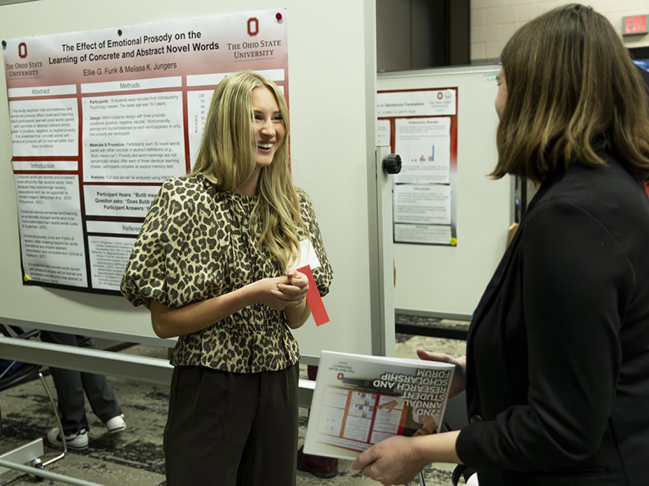 A smiling Ellie Funk stands in front of her poster presentation speaking to a faculty member during the Student Research and Creative Inquiry Forum.