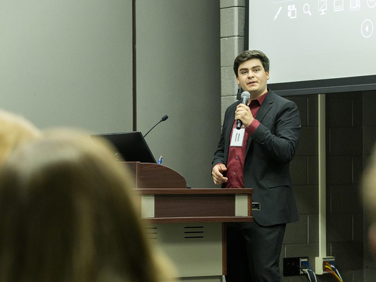 Mitchell Mazzone speaks into a microphone at a podium during his oral presentation at the Student Research and Creative Inquiry Forum.