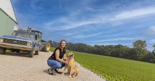 Madi Layman poses with a dog in front of a barn and field of soybeans.