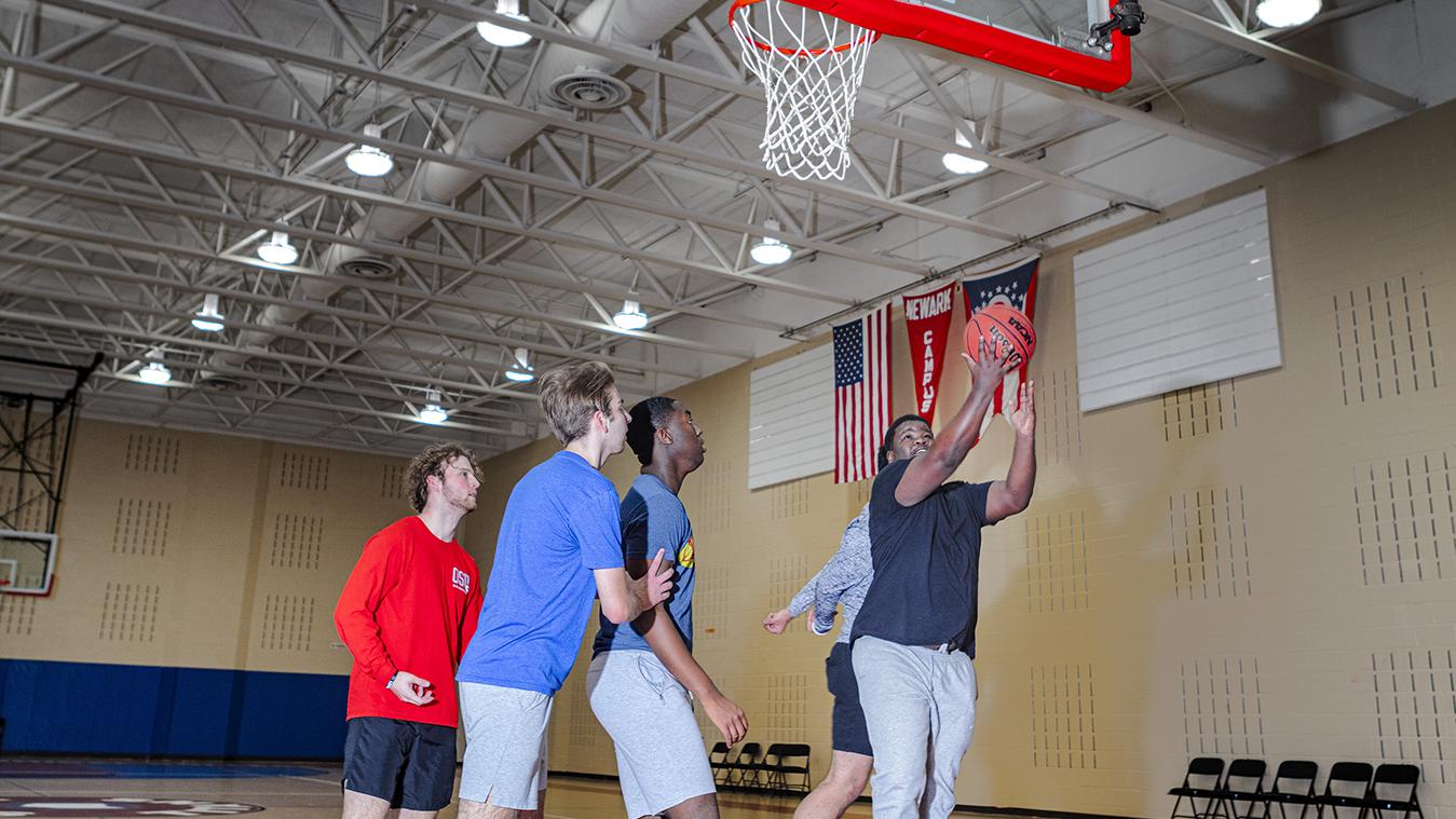 A student attempts a layup surrounded by other students during a basketball game.