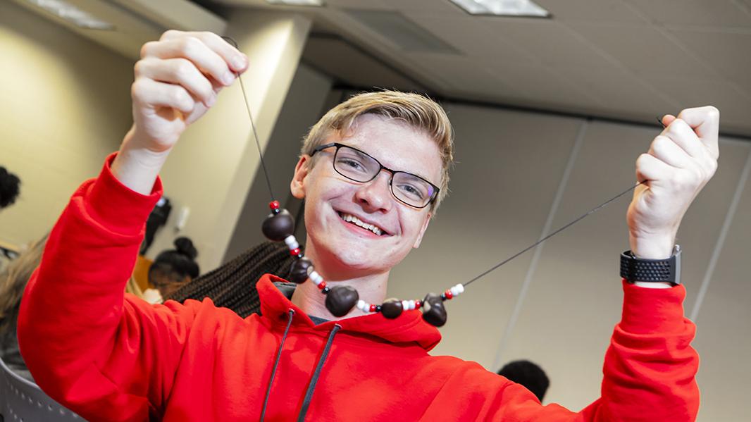 A male student holds up buckeyes that he's strung for a necklace.