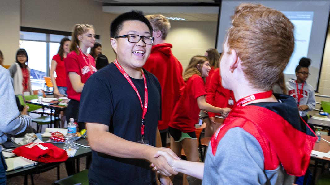Two students greet each other with a handshake.