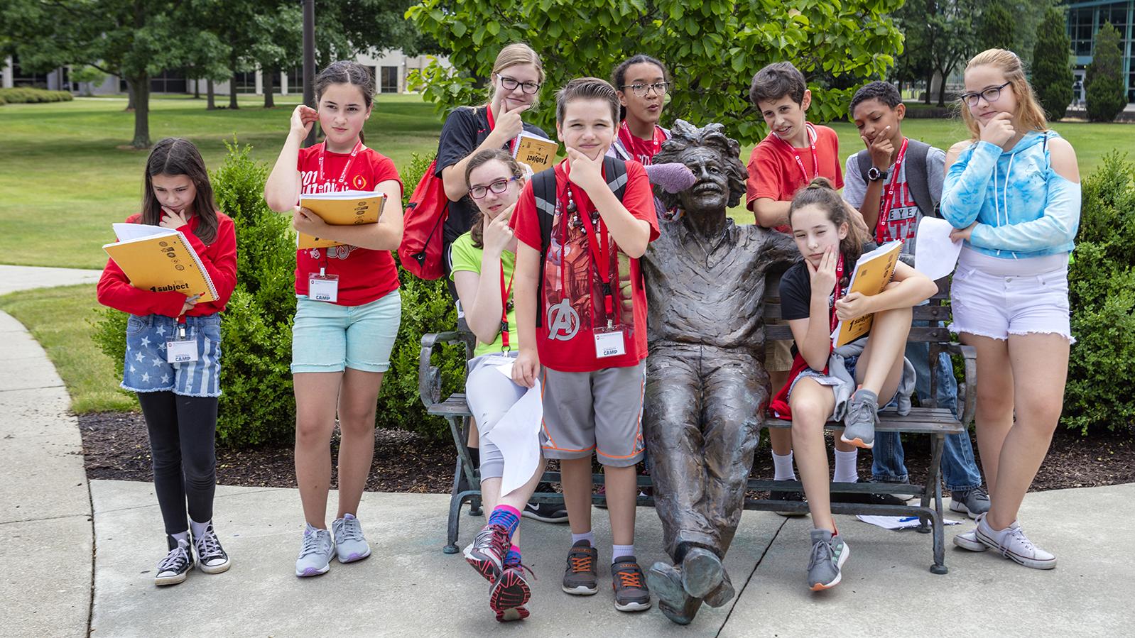 A group of students gathers around a bronze sculpture of Albert Einstein with their hands on their chin as if in thought. 