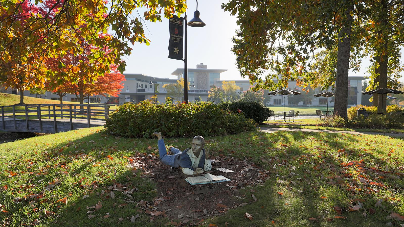 A statue of a girl who lies in the grass and writes in a notebook.