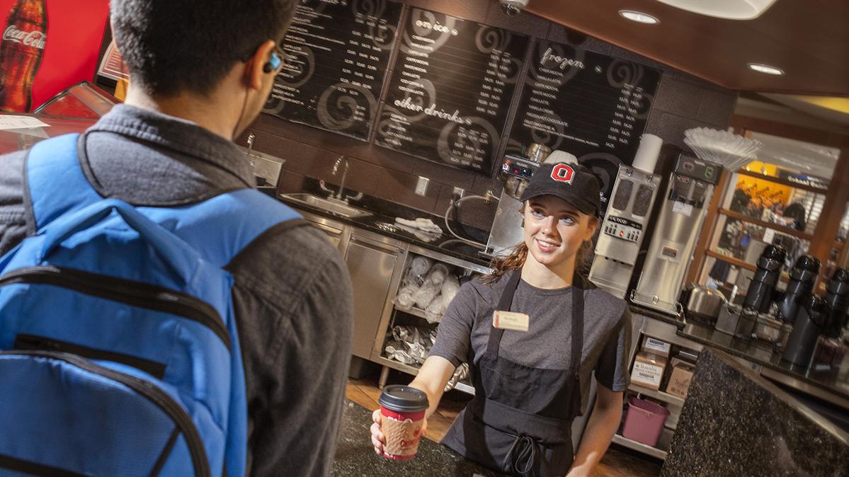 A student employee at the Bean counter hands a coffee cup to a student customer.
