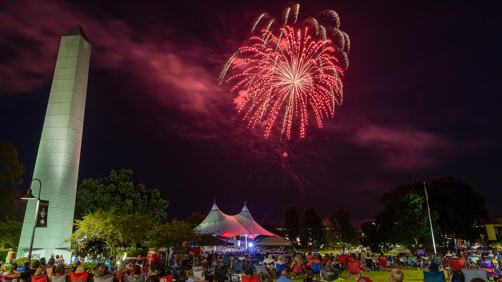 A red firework lights up the sky over a crowd of people on the Newark campus.