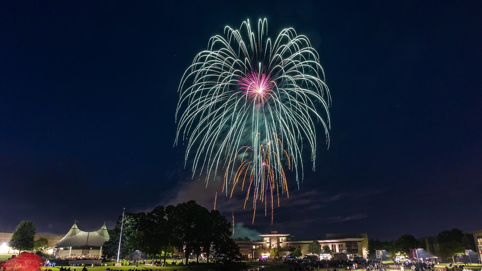 A firework fills the night sky over the Warner Center as onlookers fill the campus grounds