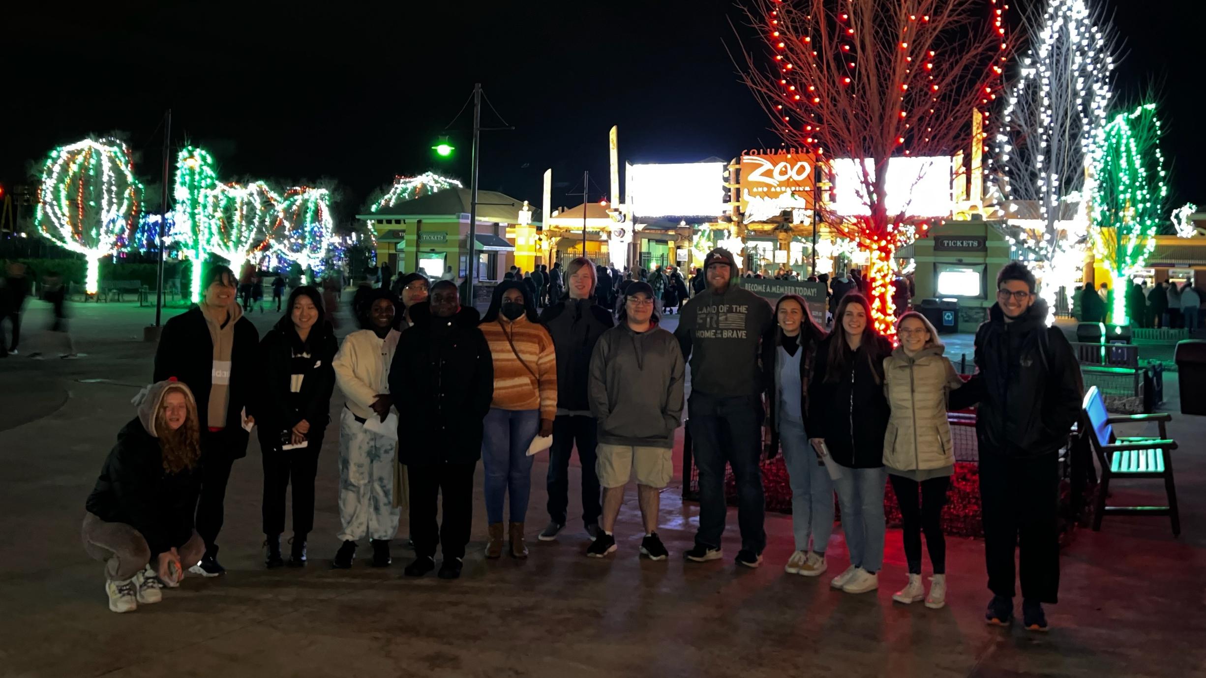 Students stand in front of trees lit for Christmas at the Columbus Zoo and Aquarium.