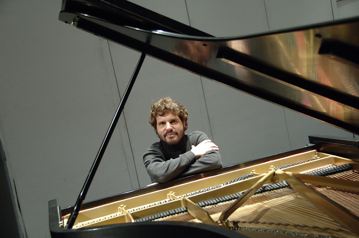 Steven Glaser sits behind a piano with his arms crossed, resting on top.