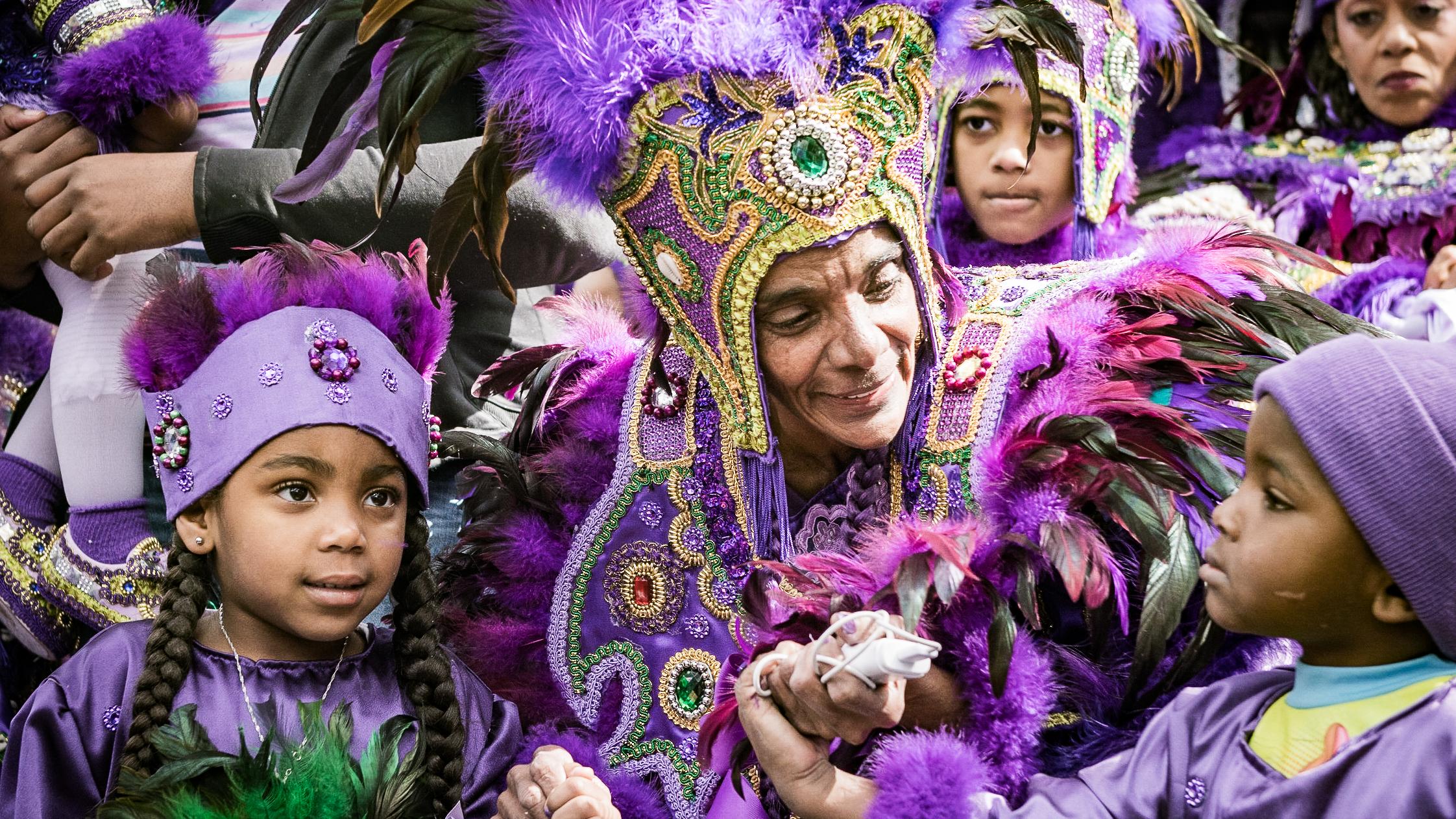 A person dressed in a beaded and feathered costume surrounded by children in similar costume.