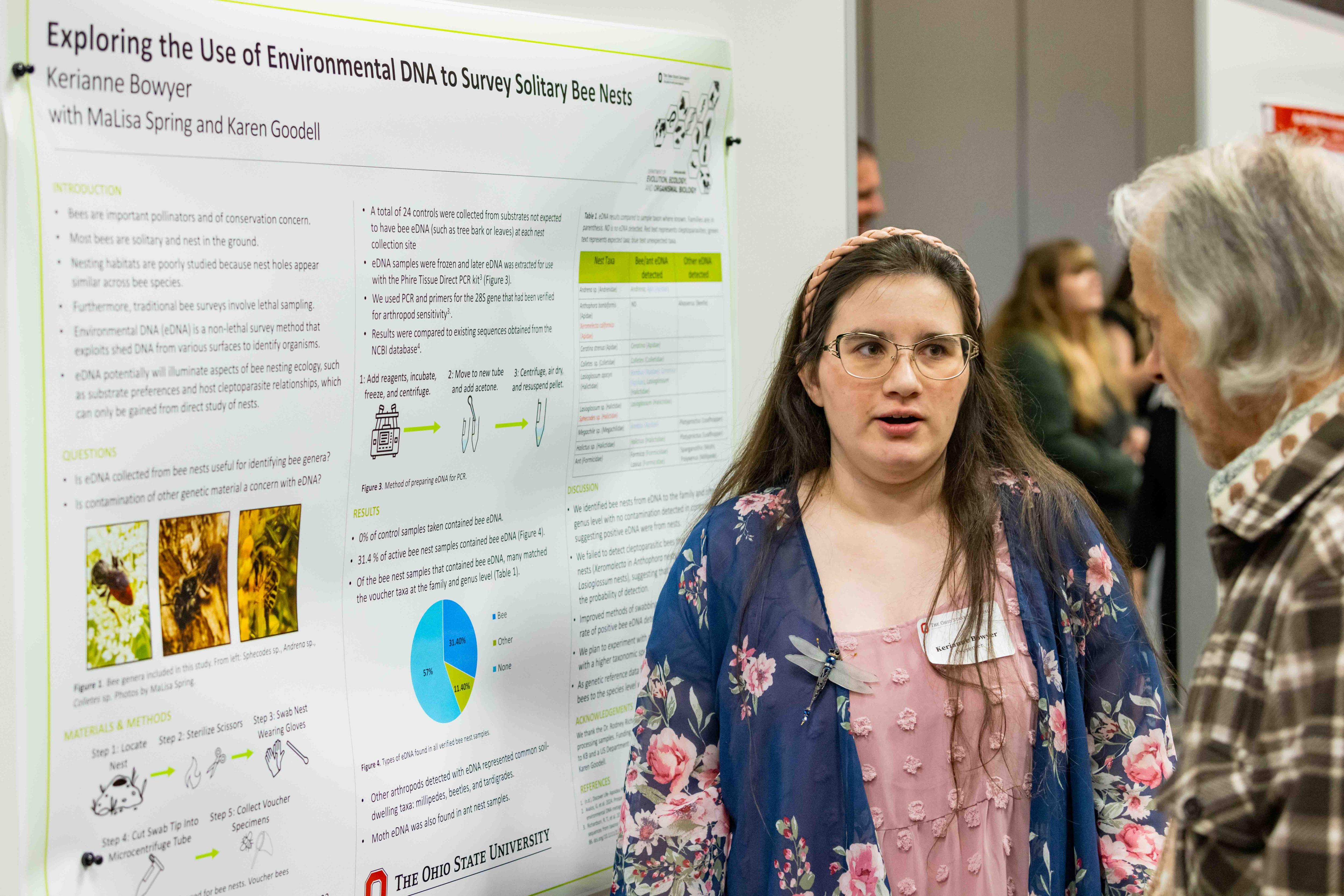 A student stands next to her poster presentation talking to a spectator. 