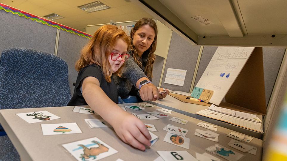 An instructor points to a card on a table as a young child places a flash card.