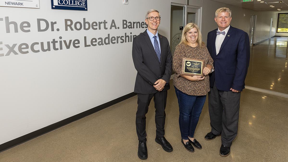 Greenstein Award recipient Amy White stands between Ohio State Newark Dean and Director Matthew Smith and COTC President John Berry holding her award plaque. 