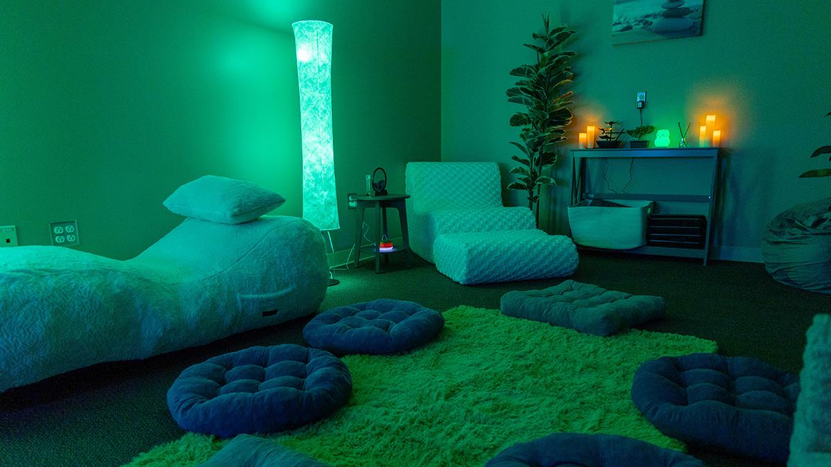 A darkened room with lounging chairs and pillows on the floor lit by candles.