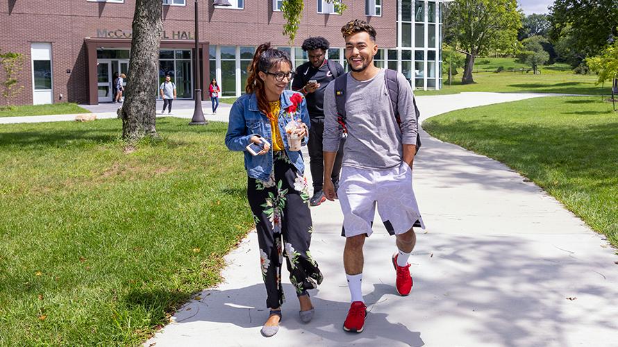 A female student and a male student walk side-by-side in conversation outside of the residence hall on campus.