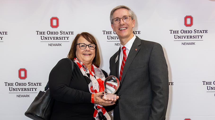 Jodie Wheeler holding her Distinguished Alumni Award stands with Ohio State Newark Dean and Director Matt Smith.