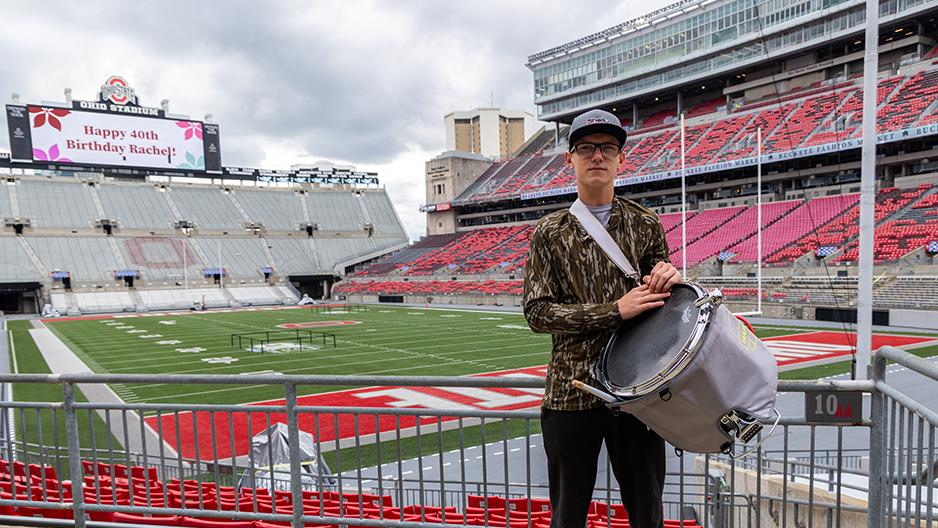 An Ohio State Newark student in Ohio State's marching band stands inside Ohio Stadium where the band plays at home football games holding his drum.