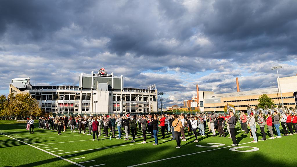 The Ohio State marching band practices on the Ohio State campus with Ohio Stadium in the background.