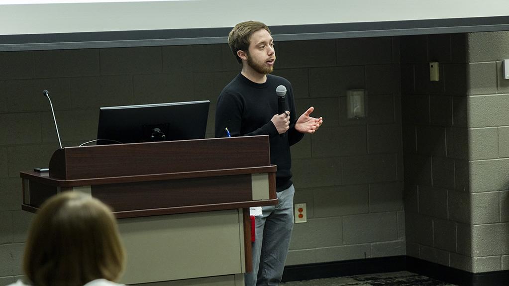 Brenden Justice stands at a podium speaking into a microphone during his oral presentation at the Student Research and Creative Inquiry Forum.