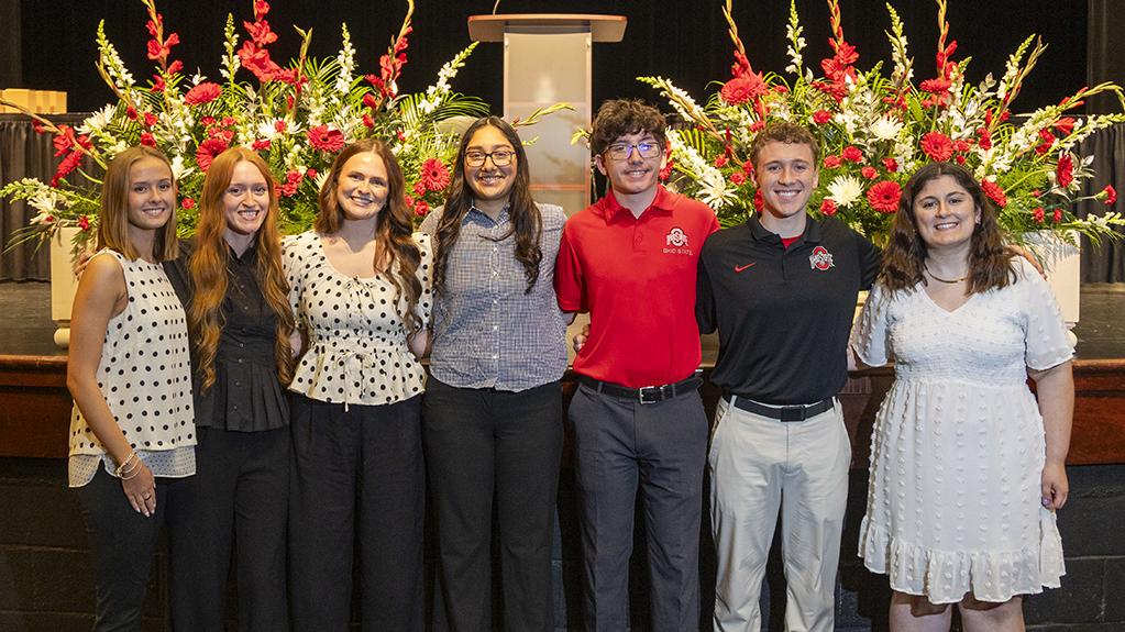 Students receiving awards at the 2025-26 graduation celebration stand in line in front of the stage with the Ohio State Newark seal in the background.