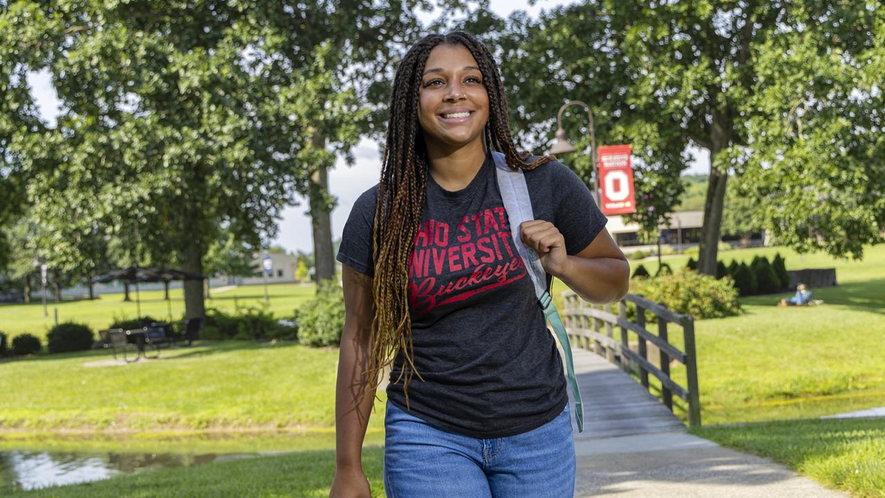 A student walks on campus smiling toward the sky. 