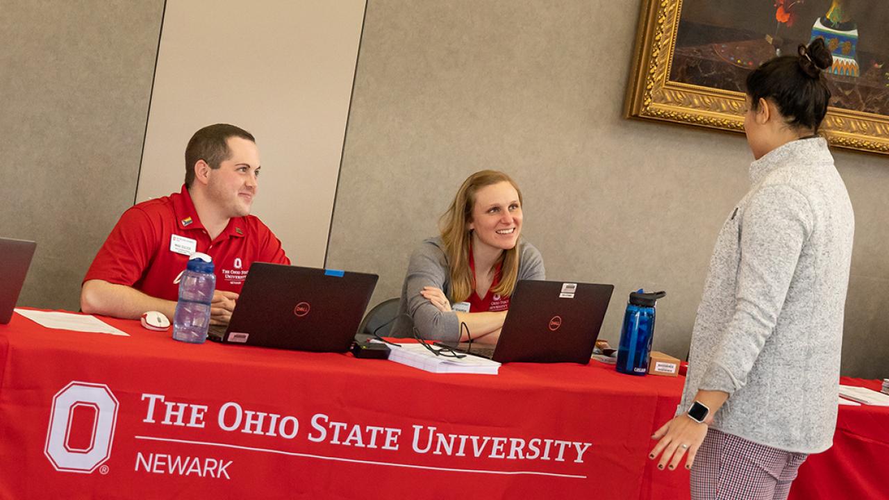 Academic advisors sit at a table talking to a student during an on-campus event.