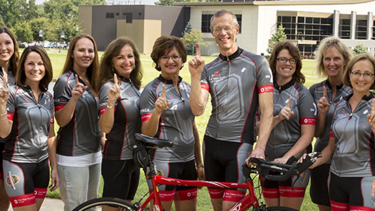 Pelotonia team in coordinating Ohio State grey cycling uniforms facing the camera, signaling "1"